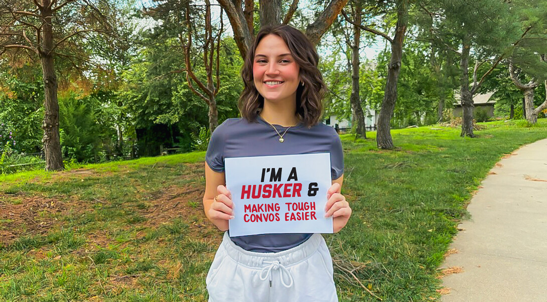 A young woman holding a sign that read, I'm a Husker & Making Tough Convos Easier