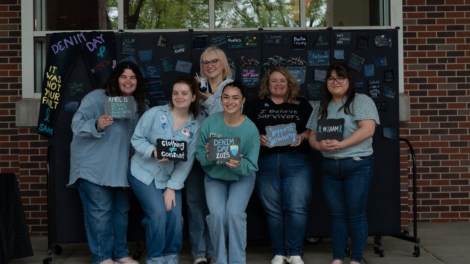 The CARE staff poses for a group photo in front of their Denim Day display in April 2025.
