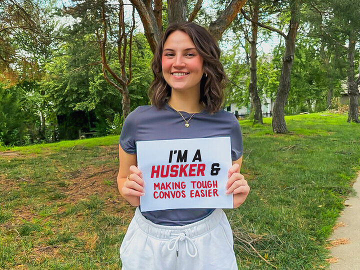 A young woman holding a sign that read, "I'm a Husker & Making Tough Convos Easier."